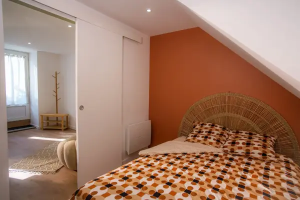 Chambre 1 : vue d’ensemble avec mur accent orange sous rampant, pièce lumineuse